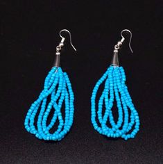 two pairs of blue beads are hanging from silver earwires on a black surface