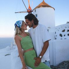 a man and woman standing next to each other in front of a white building near the ocean