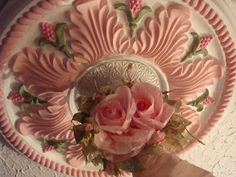 a person holding a pink flower in front of a plate with flowers on the rim