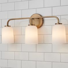 a bathroom light with three lights on it and white tiles in the wall behind it