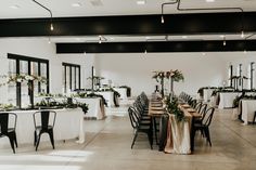 a room filled with tables and chairs covered in white tablecloths, flowers and greenery