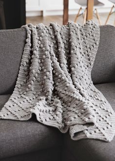 a gray couch with a knitted blanket on it's back next to a coffee table