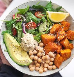 a person holding a bowl filled with vegetables and chickpeas next to a lemon wedge