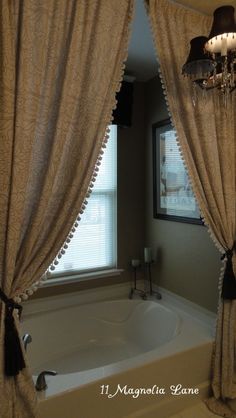 a bath tub sitting under a window next to a chandelier