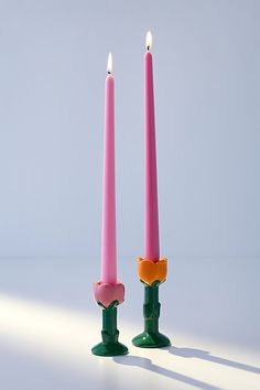 two pink candles sitting next to each other in front of a white wall with shadows on the floor