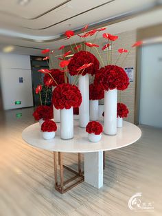 red flowers are arranged in white vases on a round table at the entrance to an office