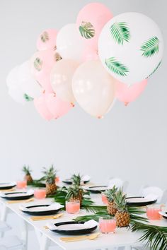 a table topped with lots of balloons and pineapples on top of white plates