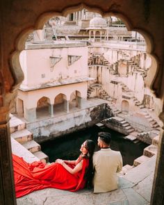 a man and woman sitting on top of a building next to each other in red dresses