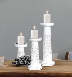 three white candles sitting on top of a wooden table