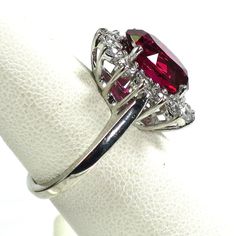 1970s Sterling and synthetic ruby cocktail ring. Oval faceted synthetic ruby in a shallow basket setting surrounded by a halo of clear CZs, atop a simple smooth shank. The stone is absolutely spectacular, a rich, saturated, delicious ruby red with glints of pink and purple deep within. The brilliant clear CZs surrounding it frame and accentuate its deep resonant hue. A perfect cocktail ring for any occasion, fancy or otherwise! Signed "Sterling". Face of ring, 0.65"L x 0.6"W. Size 6.5 Dazzling Oval Ruby Ring, Classic Oval Lab-created Ruby Diamond Ring, Formal Oval Ruby Ring With Center Stone, Dazzling Oval Ruby Ring With Prong Setting, Formal Oval Lab-created Ruby Ring, Classic Red Oval Cluster Ring, Dazzling Oval Ruby Ring With Halo Setting, Formal Oval Ruby Ring With Prong Setting, Classic Oval Lab-created Ruby Ring