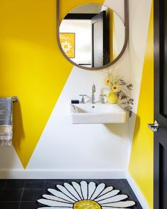 a bathroom with yellow and white walls, black tile flooring and a round mirror on the wall