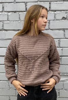 a woman standing in front of a brick wall with her hands on her hips and looking off to the side