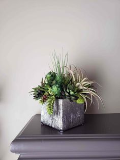 a silver planter with succulents on top of a black table next to a white wall