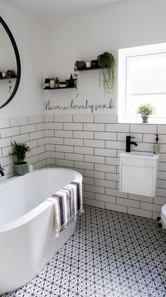 a white bath tub sitting next to a toilet under a window in a bathroom with black and white tiles