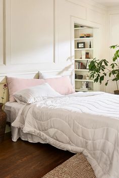 a bed with white sheets and pink pillows in a room next to a book shelf