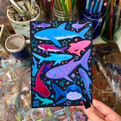 a person holding up a card with dolphins and stars on it in front of paintbrushes