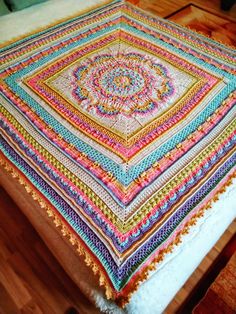 a multicolored crocheted blanket sitting on top of a wooden floor next to a bed