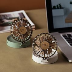 two small metal fans sitting on top of a desk next to a laptop and mouse