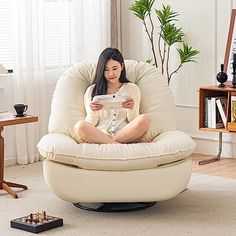 a woman sitting in a chair reading a paper while holding a remote control and looking at her phone