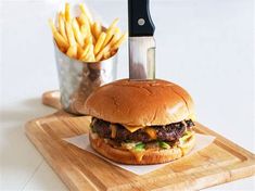 a cheeseburger with fries and a knife on a cutting board