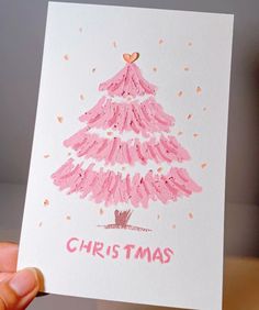 a hand holding up a christmas card with a drawing of a pink tree on it