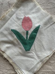 a piece of cloth with a tulip embroidered on the front and side, sitting on top of a bed