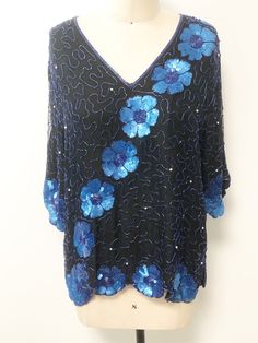 This is a beaded silk top. The random design is done with iridescent cobalt blue bugle beads. The large flowers are made up of the same beads with the petals done in sequins. There are also round silver beads interspersed front and back. My favorite part of this top is the scalloped effect the flowers give to the sleeves and hemline. A unique touch. No size tag, fits like a M/L with no stretch. Check measurements carefully. Lined with rayon. Length 26 inches Underarm to underarm 40 inches Waist Blue V-neck Blouse For Evening, Embellished Silk V-neck Top, Blue Silk V-neck Blouse, Elegant Blue Embellished Top, Fitted Blue Embellished Blouse, Blue Embellished Party Blouse, Festive Blue Sequined Blouse, Festive Blue Sequin Blouse, Blue Silk Evening Blouse