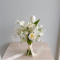 a bouquet of white flowers is sitting on a table with a ribbon tied around it