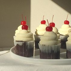 several cupcakes with white frosting and cherries on top sit on a plate