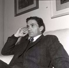 a man in a suit sitting on a couch talking on a cell phone while holding his hand to his ear