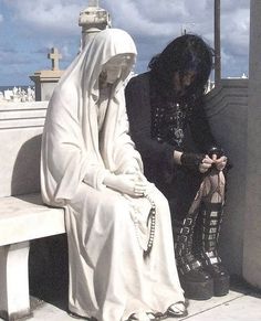 a woman sitting on top of a white bench next to a man in a black suit