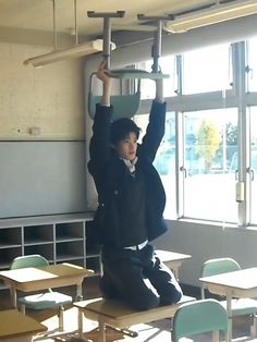 a young man sitting on top of a wooden table in front of a classroom filled with desks