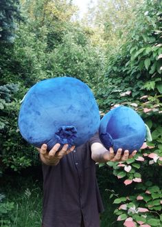 a man holding two large blue balls in front of his face with trees and bushes behind him