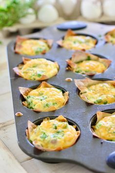 a muffin tin filled with mini quiches on top of a wooden table next to eggs