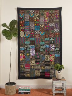 a patchwork quilt hanging on the wall next to a potted plant