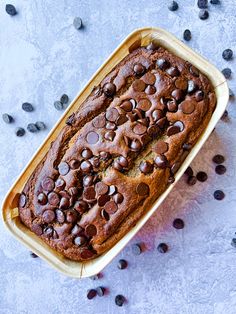 a loaf of chocolate chip banana bread in a pan on a table with chocolate chips scattered around it