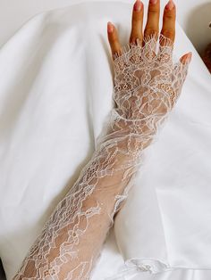 a woman's arm covered in white lace on top of a bed next to a teddy bear