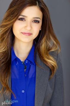 a woman with long hair wearing a blue shirt and gray blazer smiling at the camera