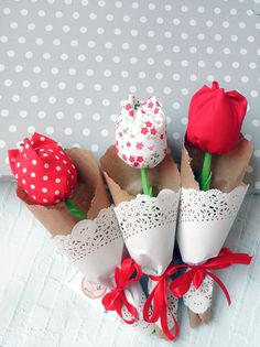 four small flowers are in paper cones with red bows on the top and white polka dot wallpaper behind them