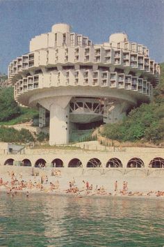 people are swimming in the water next to a building on top of a hill that looks like an ocean front