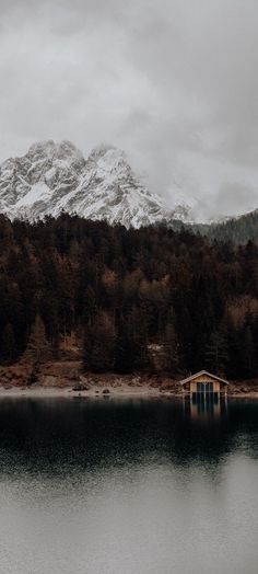 there is a boathouse on the water in front of a mountain with snow on it