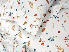 a close up of a bed with white sheets and colorful flowers on the coverlet