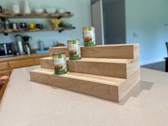 three cans of canned dog food sitting on top of a wooden shelf in a kitchen