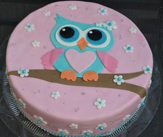 a cake decorated with an owl sitting on a tree branch and pink frosted icing