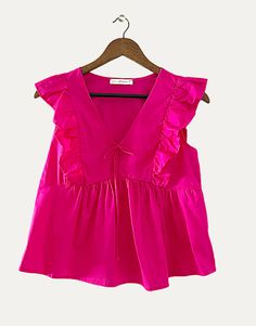 a pink top with ruffles on it hanging from a wooden hanger in front of a white wall