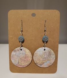 a pair of earrings with a map on it and blue beads hanging from the earwires