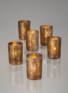 five gold votive candles sitting next to each other on a white surface with reflections