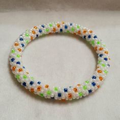 This bangle reminds me of a blooming garden with orange, green, and blue beads scattered among a shiny white background.  Made with size 8 Toho glass seed beads and crochet cotton thread. This roll-on bangle will fit a 7.5 inch wrist, but can stretch up to 1/2 inch. It measures 3/8 inch (12mm) wide. Very sturdy and flexible. If you like the design but would like different colors or measurements, please feel free to convo me. I welcome all custom orders!   This item will ship in a cotton-filled b White Beaded Bangle With Round Beads, Adjustable Beaded White Bangle, Adjustable White Beaded Bangle, Seed Bead Crochet, Garden Spiral, Blooming Garden, Cat Friendly Home, Bead Crochet, Blue Beads