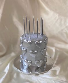 a silver cake with hearts on it and candles sticking out of the top is sitting on a plate