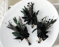 three black flowers are placed on a white plate with greenery in the center and two stems sticking out of it